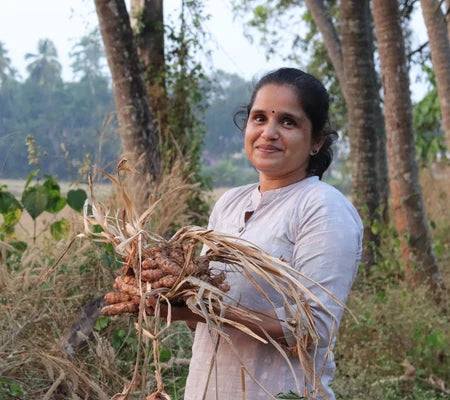 Geetha holding harvested turmeric in a natural farm setting representing a woman-led turmeric superfood brand.