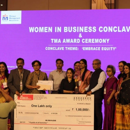 Geetha with a group of people holding a large check at a Women in Business Conclave & TMA Award Ceremony.